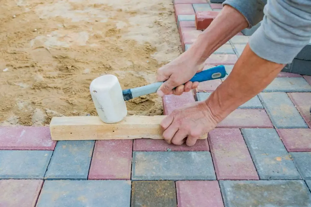 Worker leveling concrete blocks for how to seal pavers with sand project.