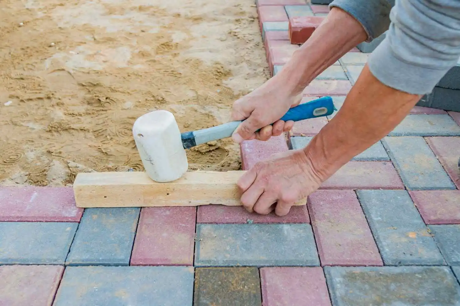 Worker leveling concrete blocks for how to seal pavers with sand project.