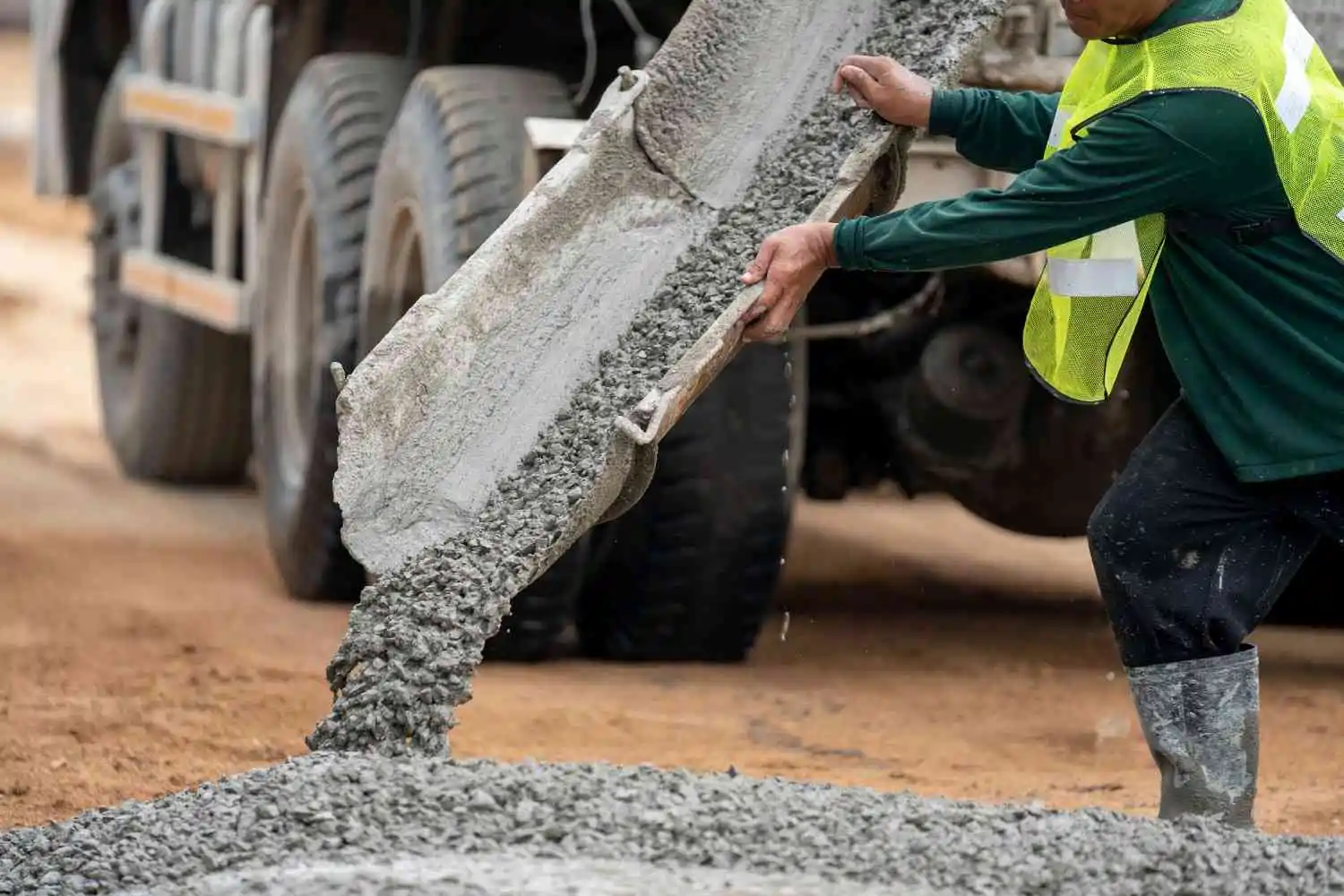 Construction worker guiding wet concrete down a mixer truck chute to illustrate how much concrete fits in a truck.