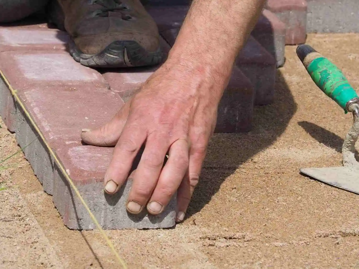 Hand placing a paving stone over sand to demonstrate what sealing pavers with sand actually means.