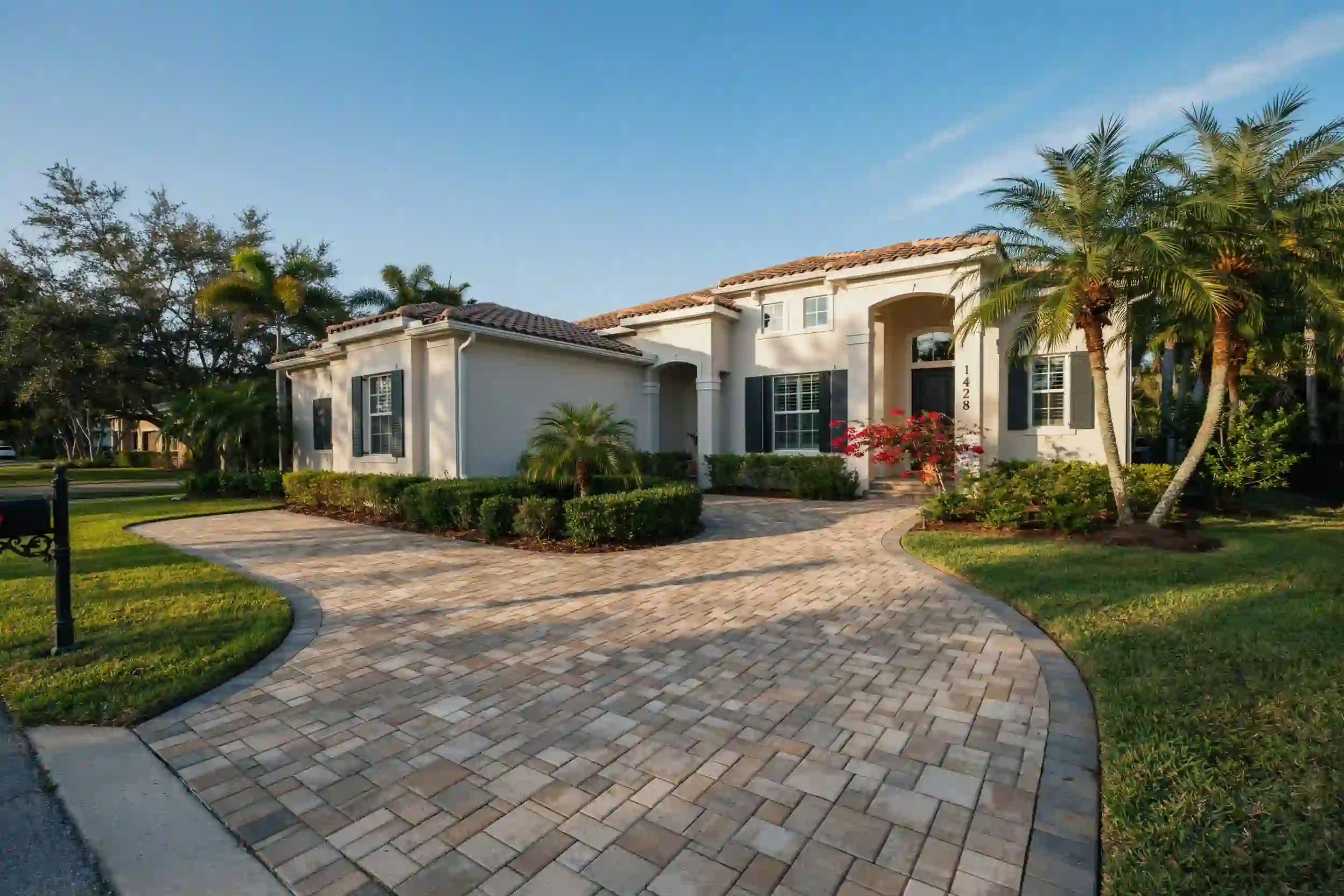 Curved paver driveway with dark border wrapping around landscaping to the front entry of a stucco home