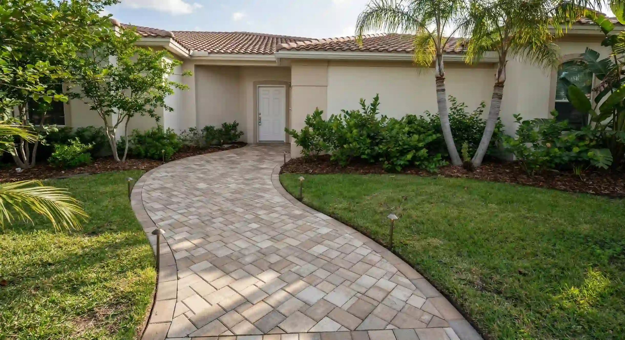 Curved stone paver walkway leading through a green lawn to a house front entrance.